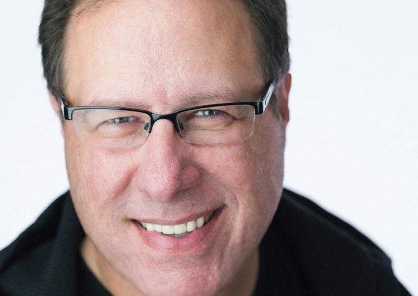 Head and shoulders portrait of Scott Kelby, smiling, wearing glasses and a dark jacket against a white background