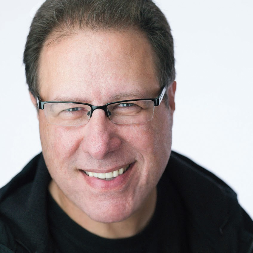 Head and shoulders portrait of Scott Kelby, smiling, wearing glasses and a dark jacket against a white background