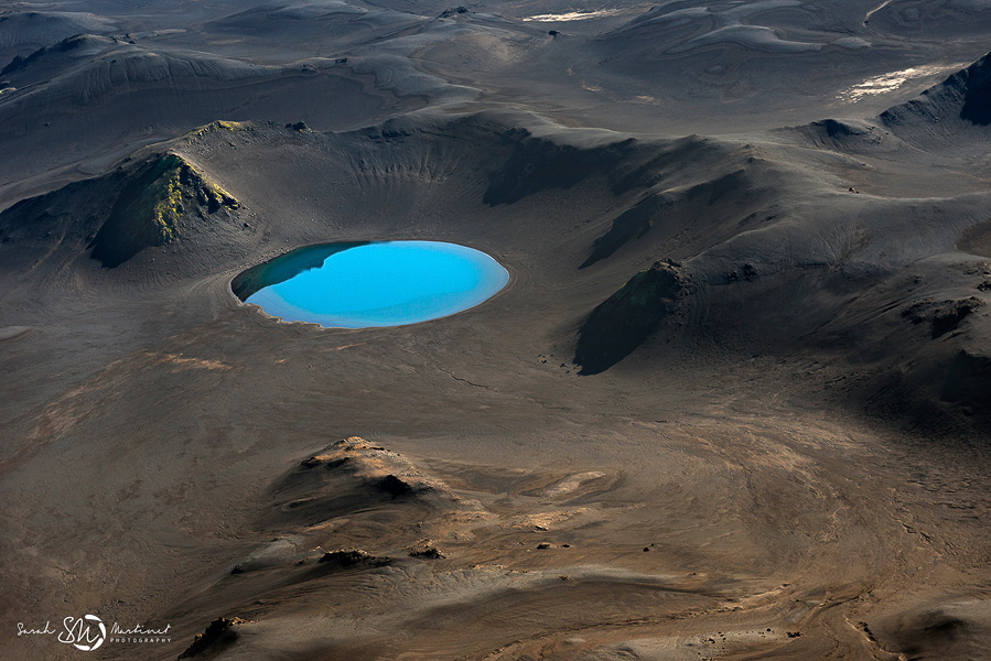 Turquoise crater lake amid dark hills
