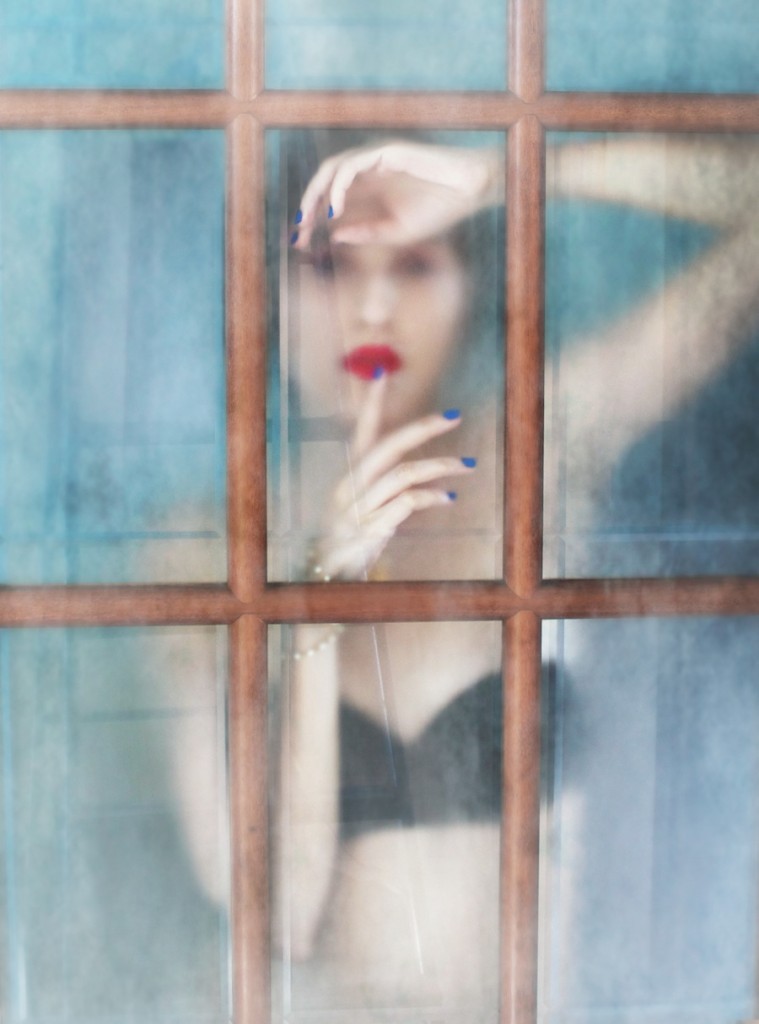 Woman seen behind a weathered blue window