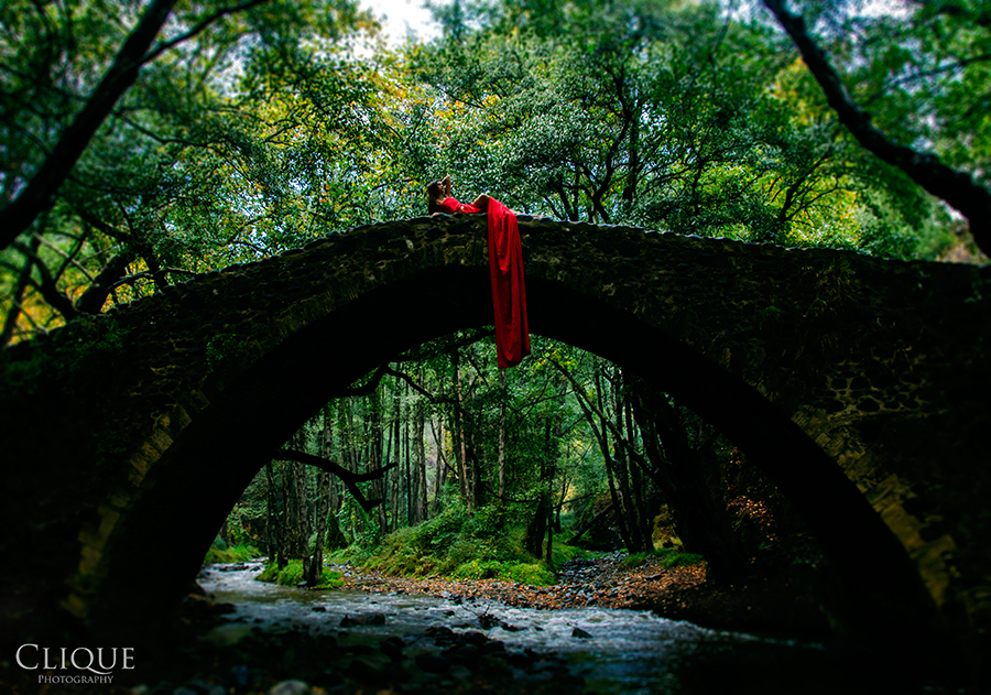 Red-dressed figure on an arched bridge in a forest