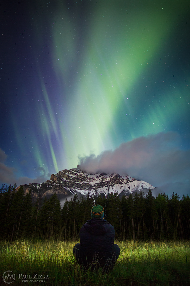 Figure beneath northern lights near dark mountains