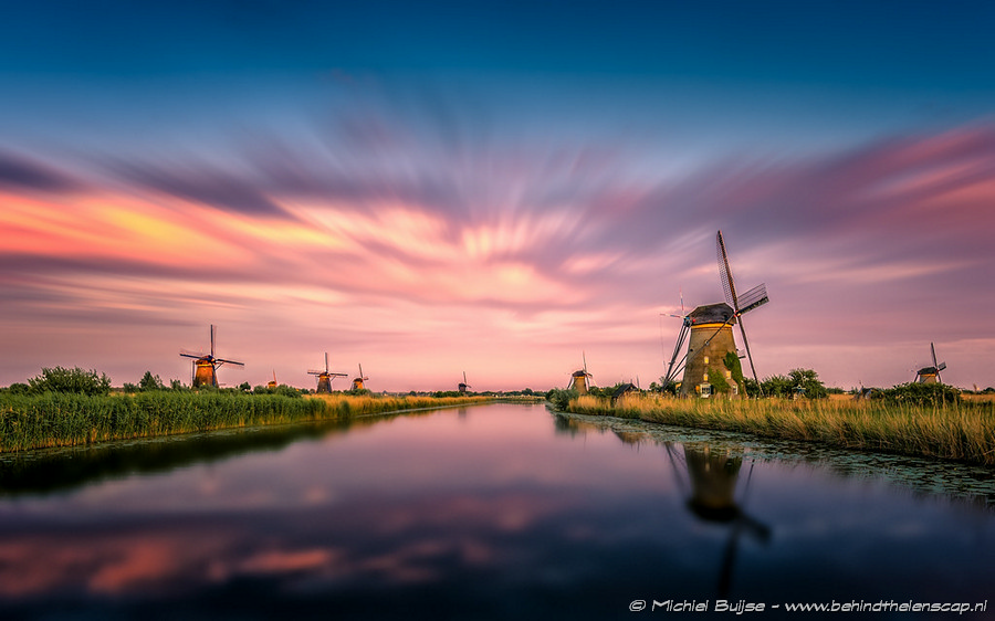 Windmill reflected in water under a pink sunset