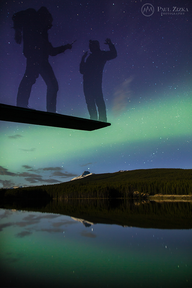 Figure beneath northern lights beside water