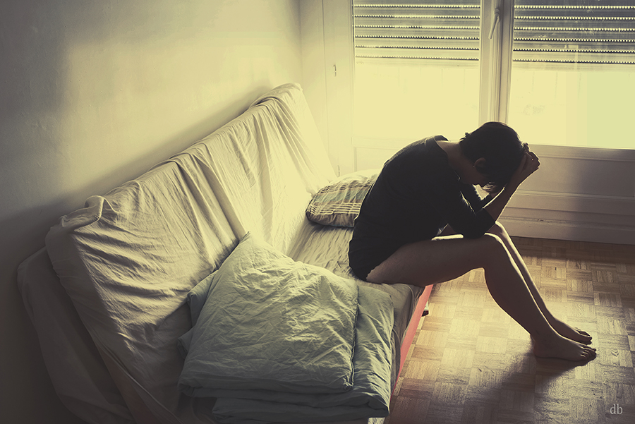 Figure curled beside a bed in soft yellow light