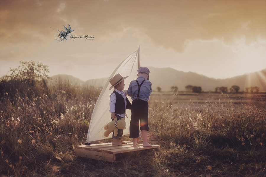 Two children beside a sailboat in a grassy field