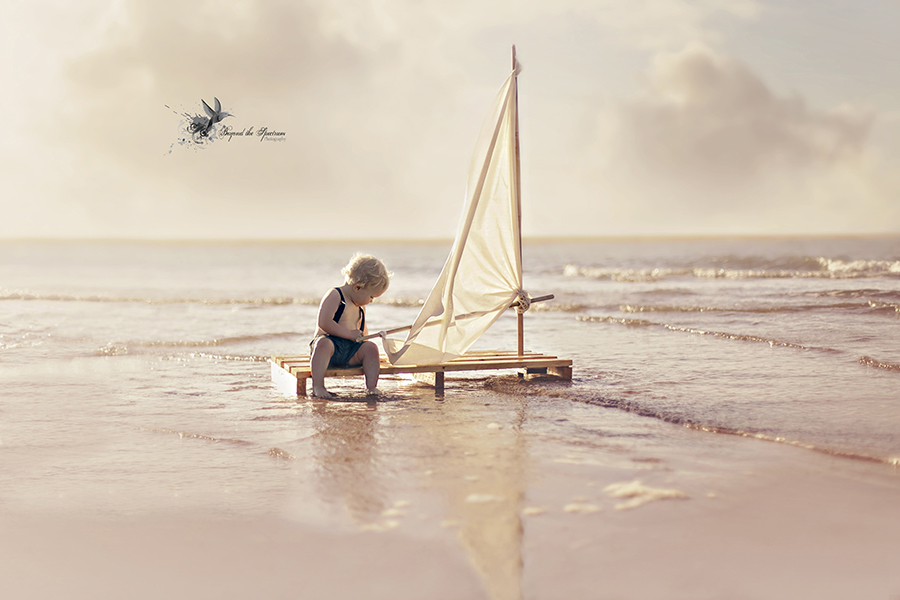 Child pushing a small sailboat at the shore