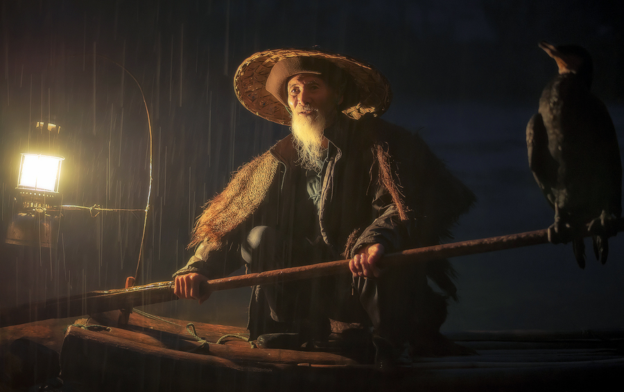 Fisherman with bird on a boat at night