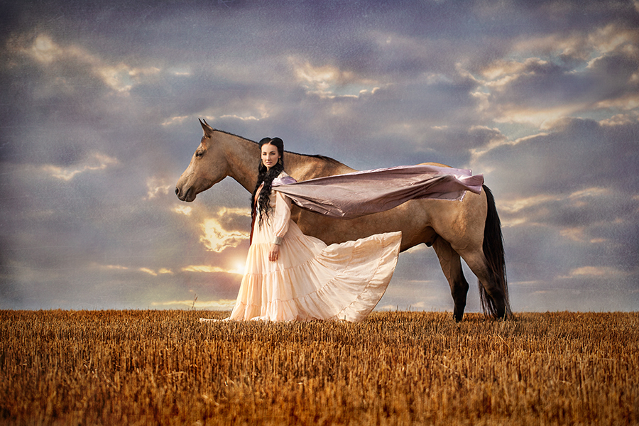 Woman holding a light fabric dress in a field under stormy sky