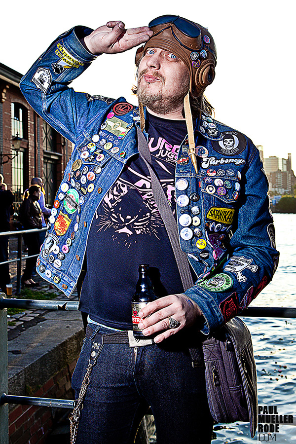 Fan in patch-covered denim jacket holding drink