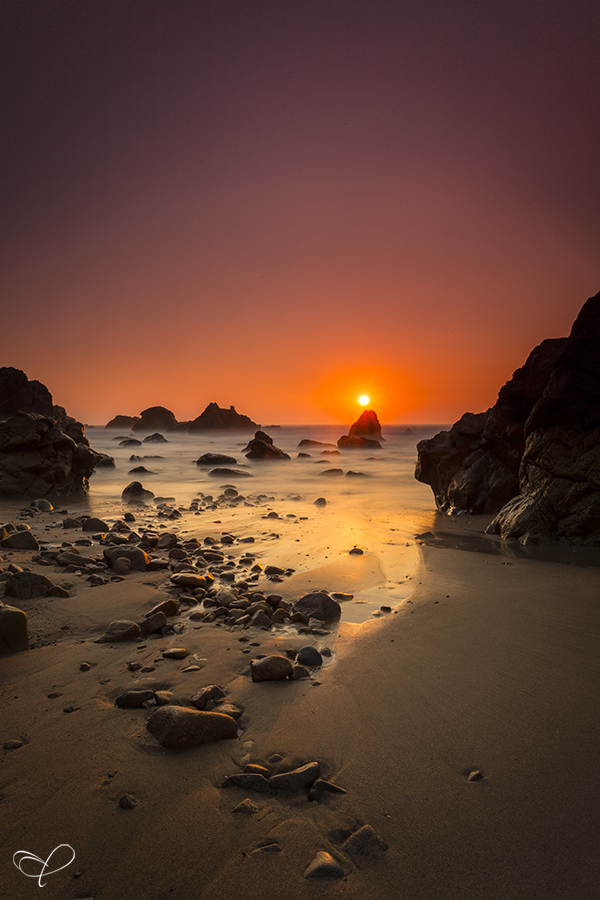 Sun setting over rocks along a beach