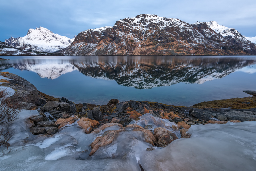 Snowy mountains reflected in water at dawn