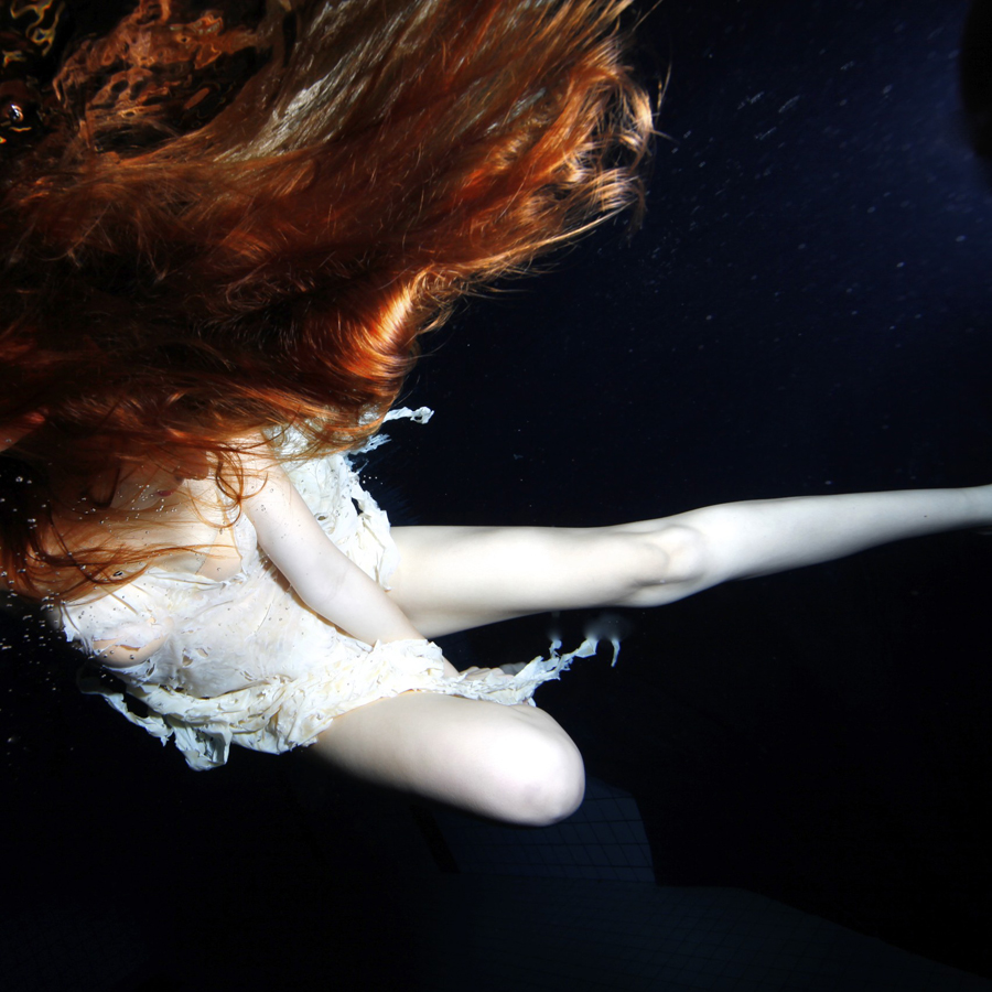 Pale figure with red fabric suspended in darkness