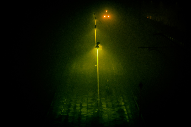 Streetlamp glowing through green night fog