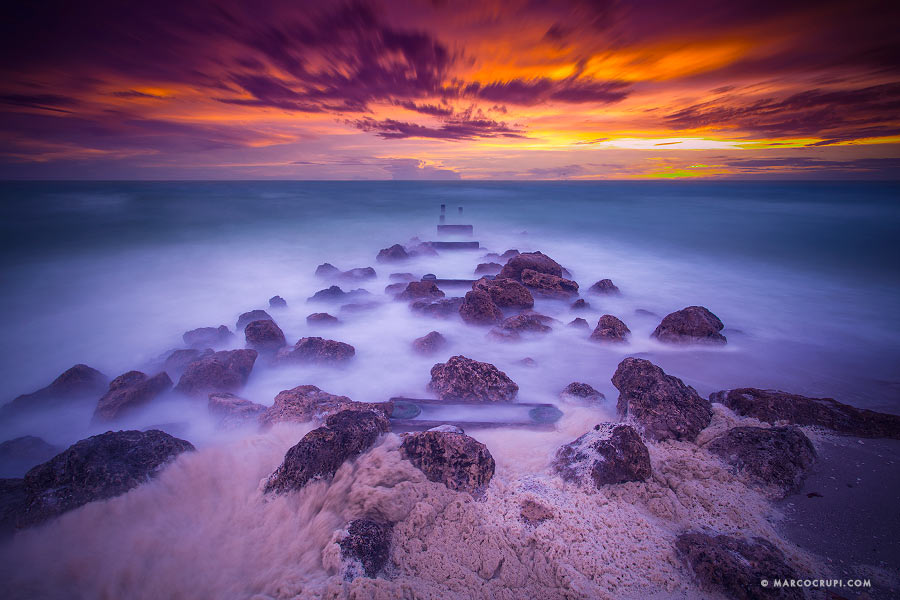 Rocks and waves beneath a purple sunset