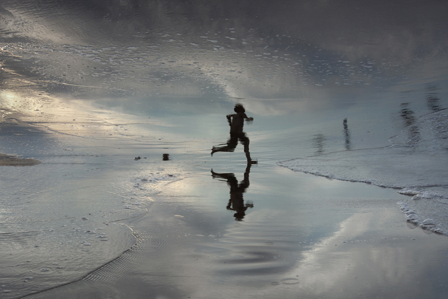 Figure running across reflective wet sand