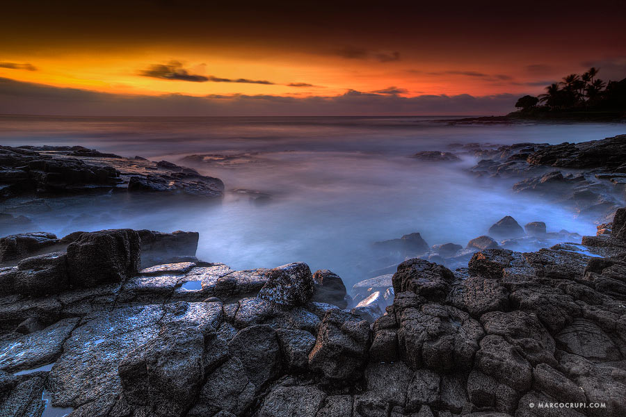 Rocky shoreline beneath an orange sunset
