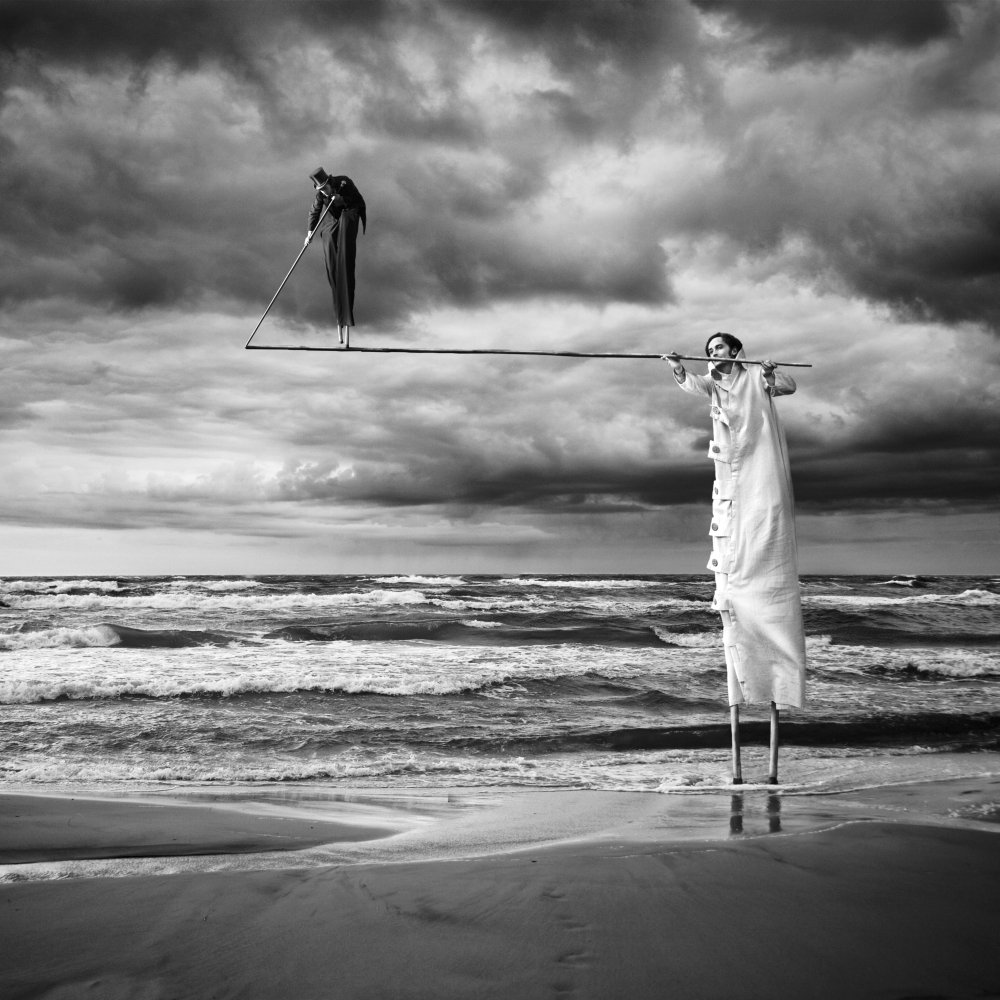 Two figures on stilts beneath dramatic clouds
