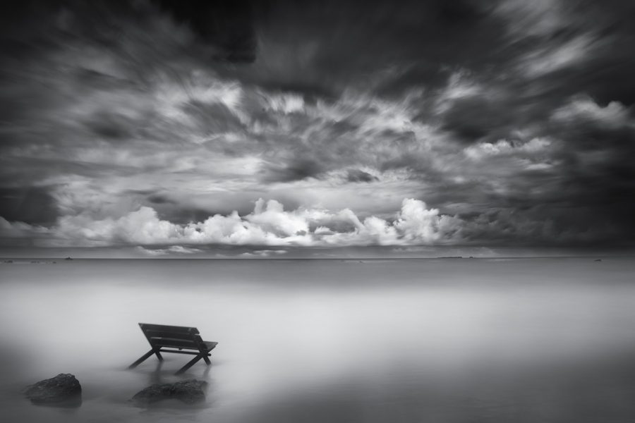 Chair standing in calm water beneath clouds