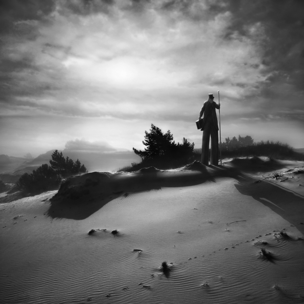 Figure standing on rocks beneath a bright sky
