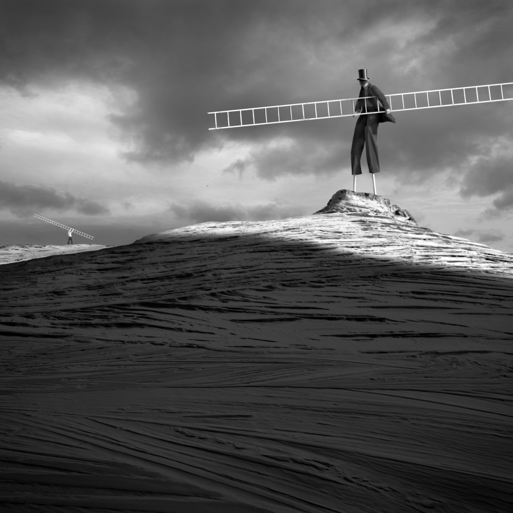 Surreal figure carrying a long ladder across sand