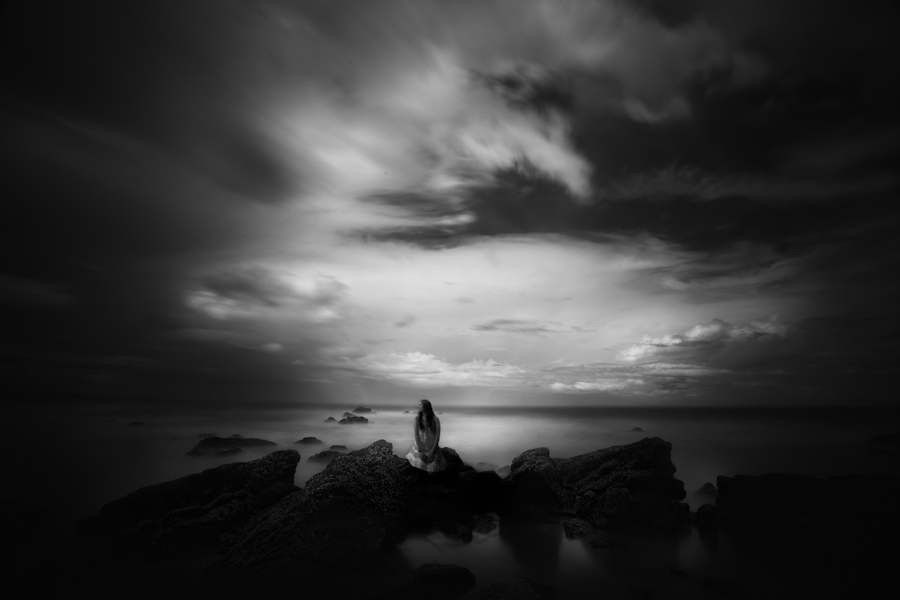 Lone figure on rocks beneath a dramatic monochrome sky