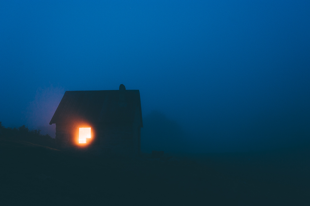 Small shelter with a warm illuminated opening in blue fog at night