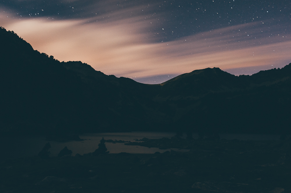 Dark mountain silhouettes beneath stars and warm bands of cloud at twilight