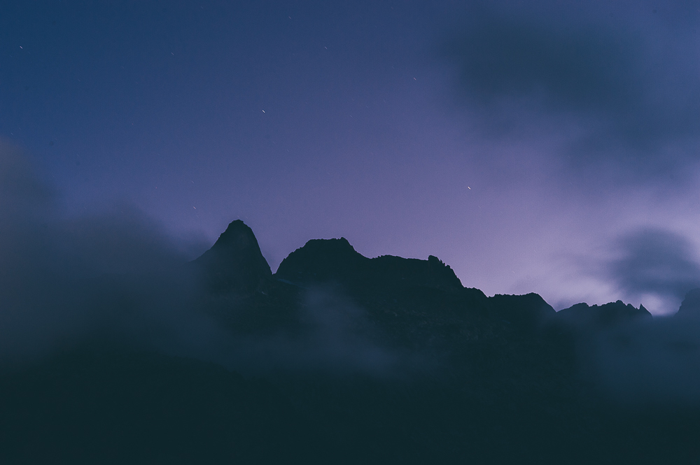 Pointed mountain ridge partly hidden by cloud beneath a violet-blue sky