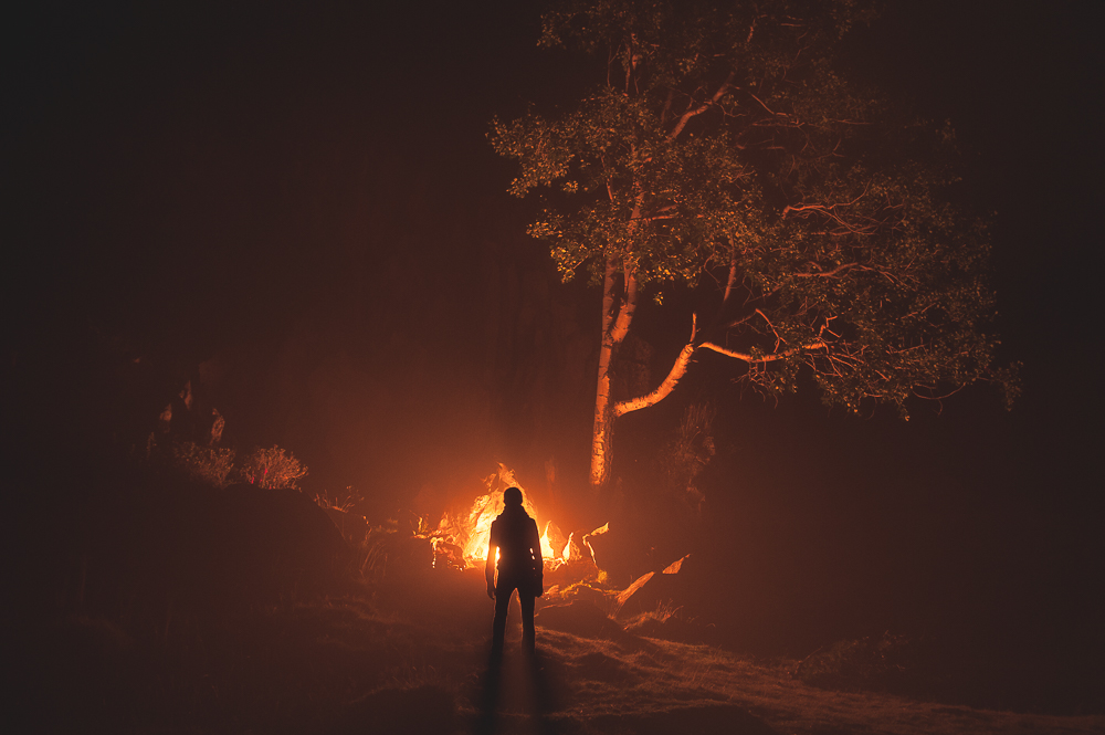 Standing silhouette beside a small warm light under a tree at night