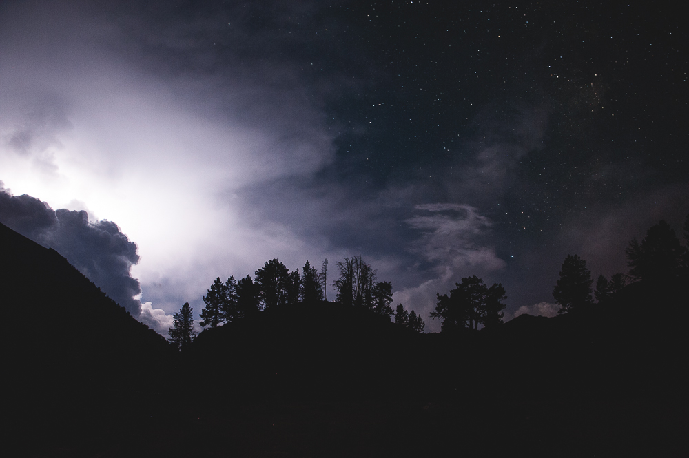 Bright cloud above dark trees and a mountain silhouette at night