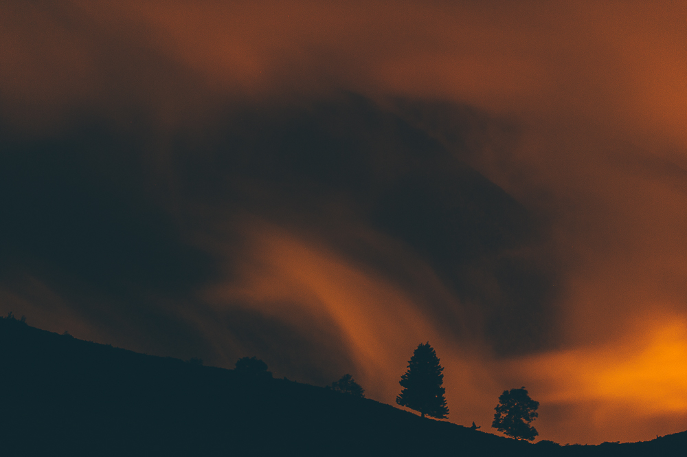 Small tree silhouettes beneath orange cloud over a dark mountain slope