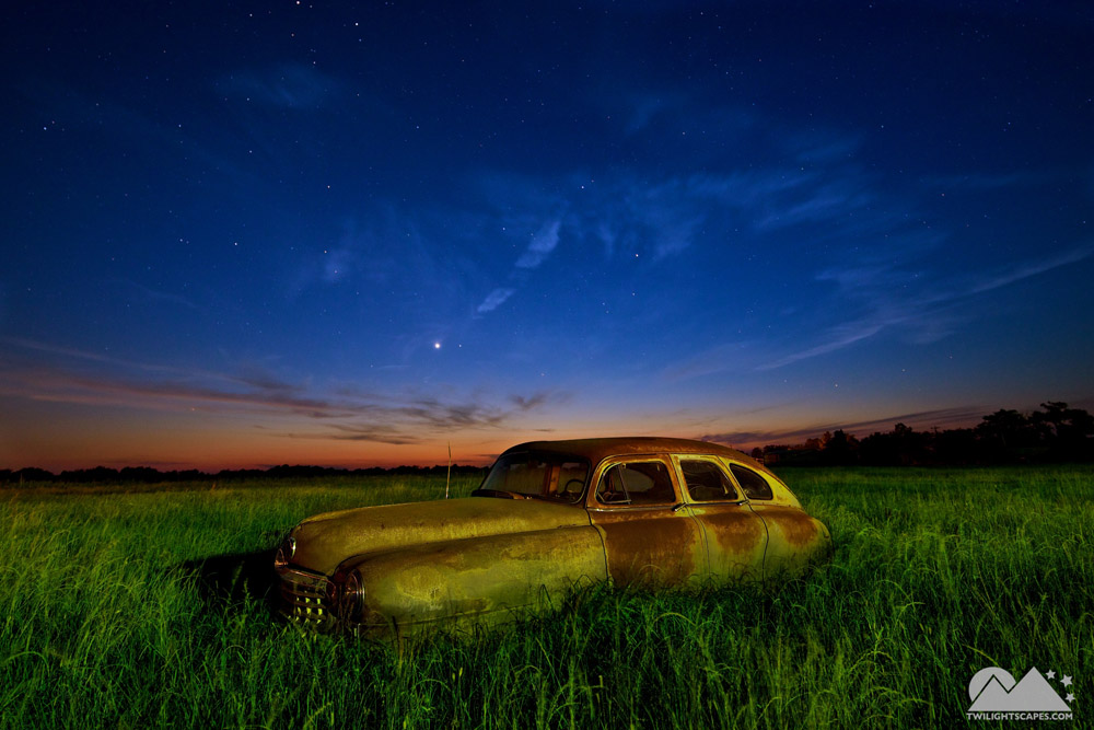 Weathered rounded automobile in a green field beneath a twilight sky