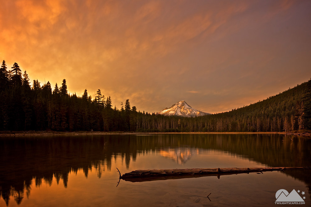 Mountain lake reflecting a tree line and distant peak beneath a warm clouded sky