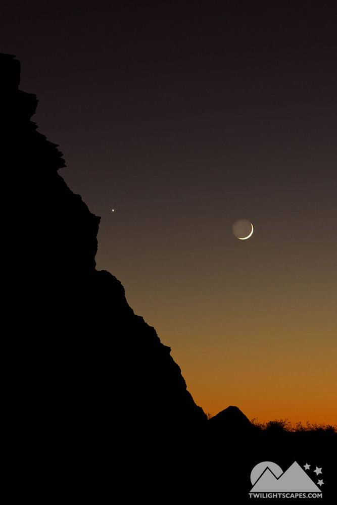 Small crescent-shaped light above a dark rock silhouette and warm low horizon