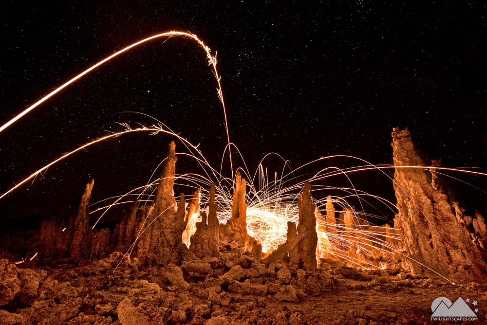 Bright curved light traces above rugged rock shapes against a dark background