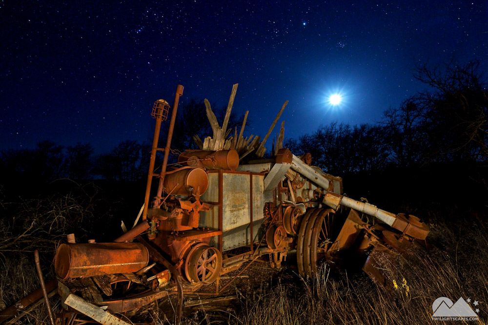 Old wheeled machinery with upright components under a bright light in the night sky