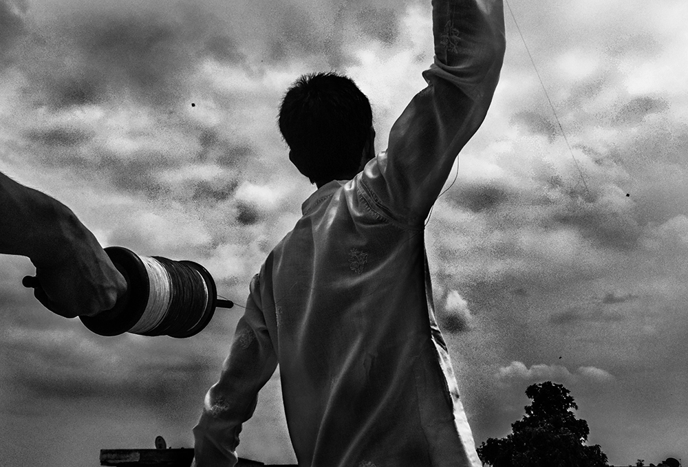 Boy flying a kite with a camera lens in the foreground, Delhi - Life by Devashish Gaur