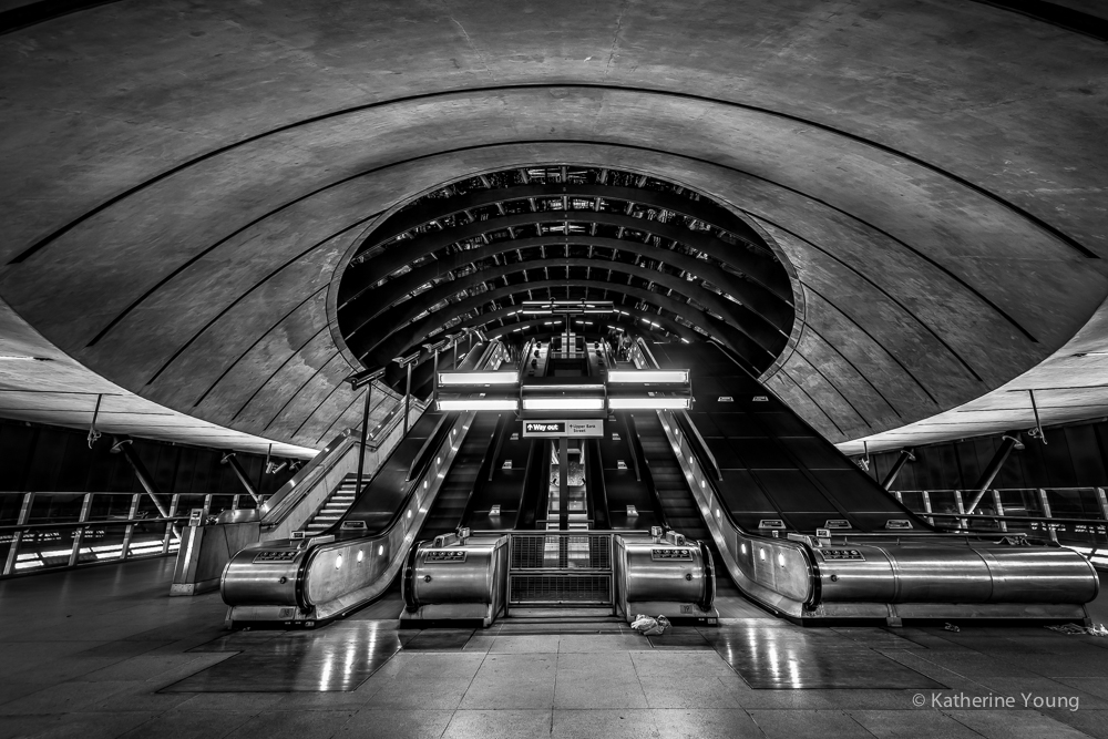 Black and white London station escalators beneath a circular concrete opening