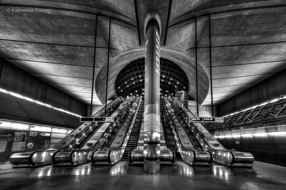 Black and white London station with central escalators and repeating curved ceiling