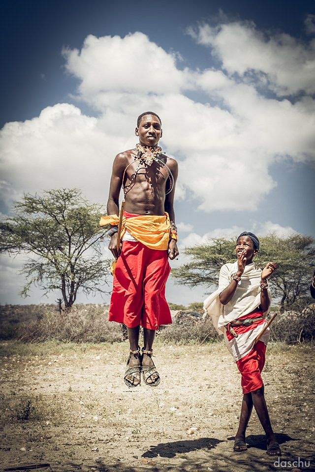 Samburu warrior leaping during a dance as a child watches - Daniel Schuhmacher