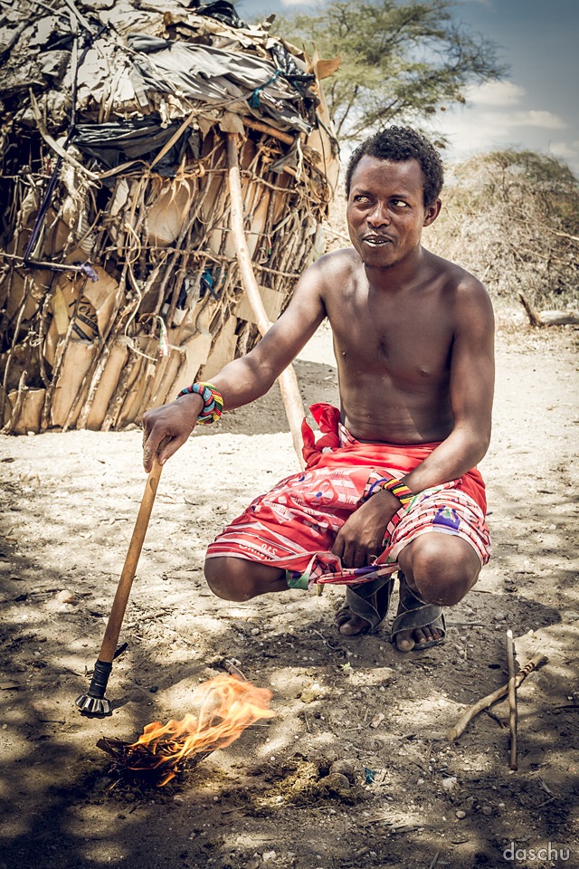 Samburu man with a walking stick by a thatched hut - Daniel Schuhmacher