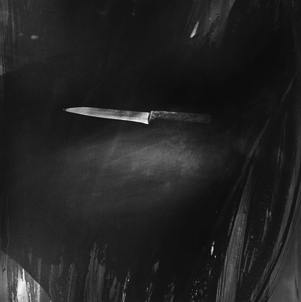 A horizontal blade-shaped object emerging from darkness in a black-and-white composition