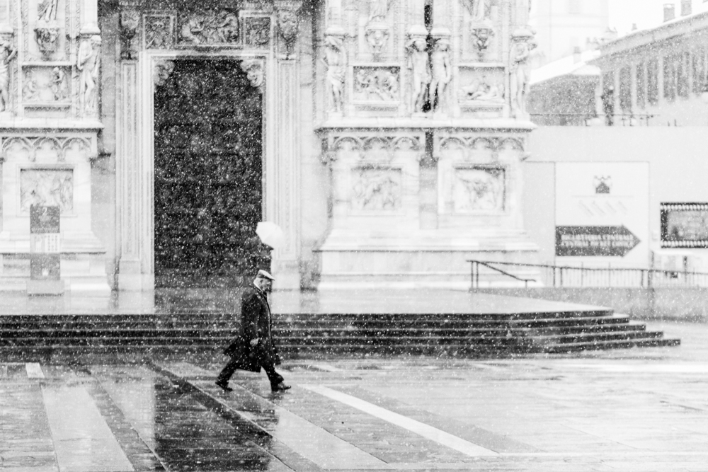 Man walking past an ornate cathedral facade in the snow - Rain by Marco Gaia