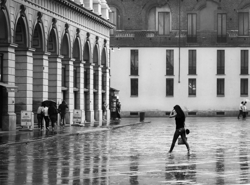 Lone pedestrian on wet pavement by an arched gallery in the rain - Rain by Marco Gaia