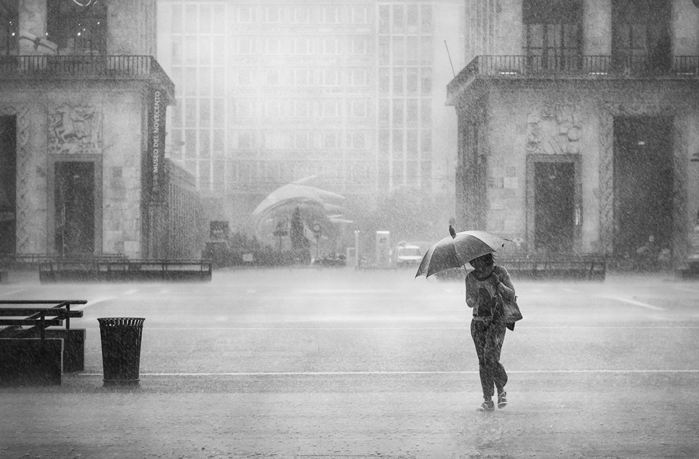 Person with an umbrella crossing a foggy square - Rain by Marco Gaia