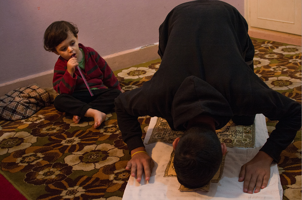 Man praying as a child watches - The Unblinking Eyes by Nensi Bogdani