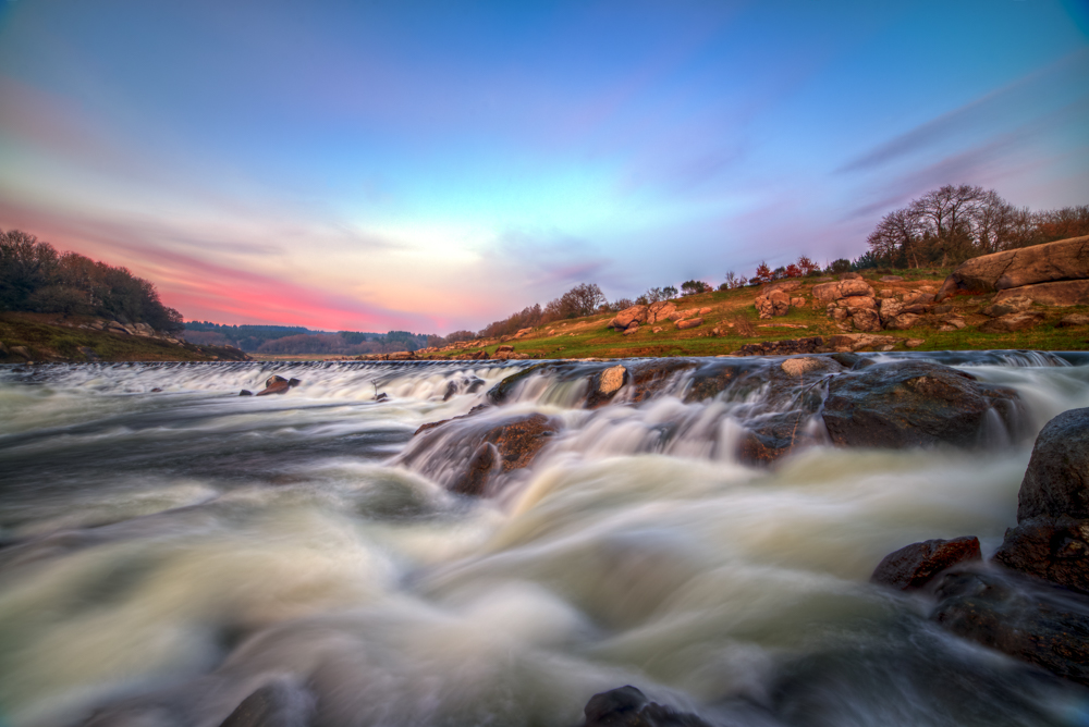 Long exposure of river rapids over rocks beneath a colorful dusk sky