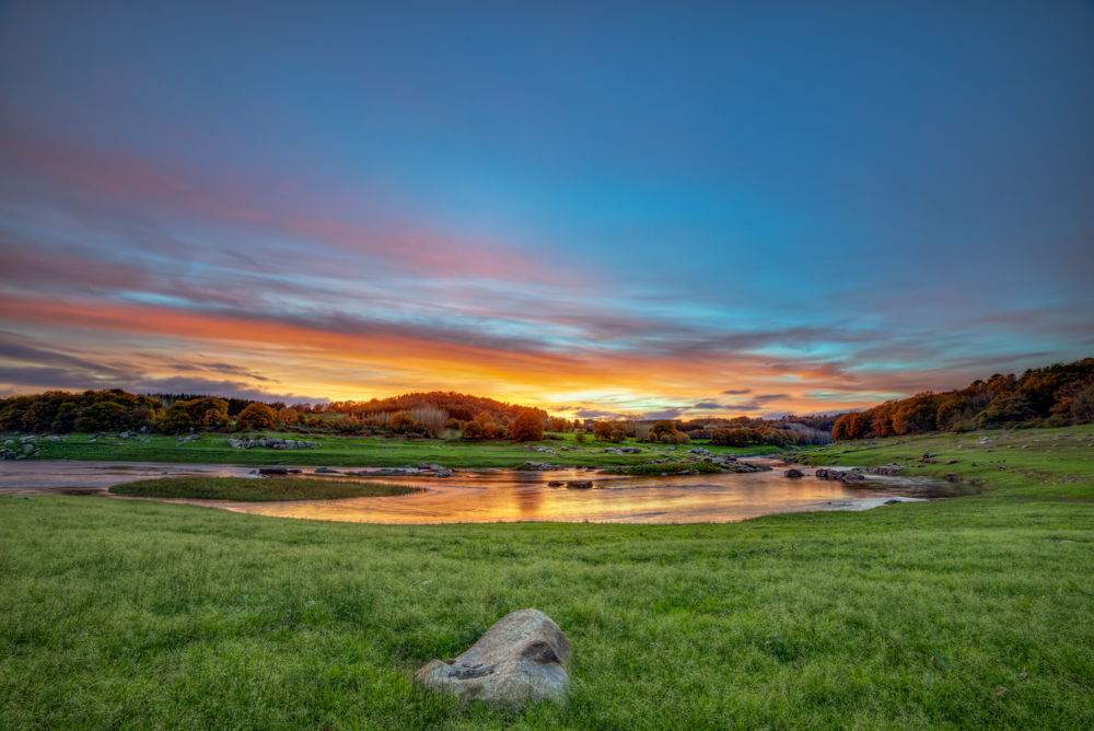 Colorful sunset sky over a green meadow and small pond in Galicia Spain