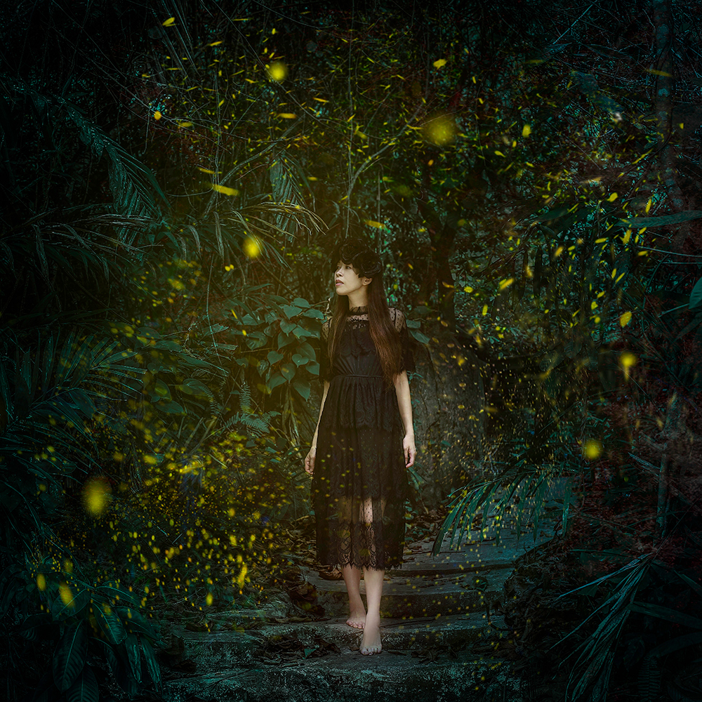 Woman in a dark dress in a green firefly forest - surreal photo by Cathryn Mok